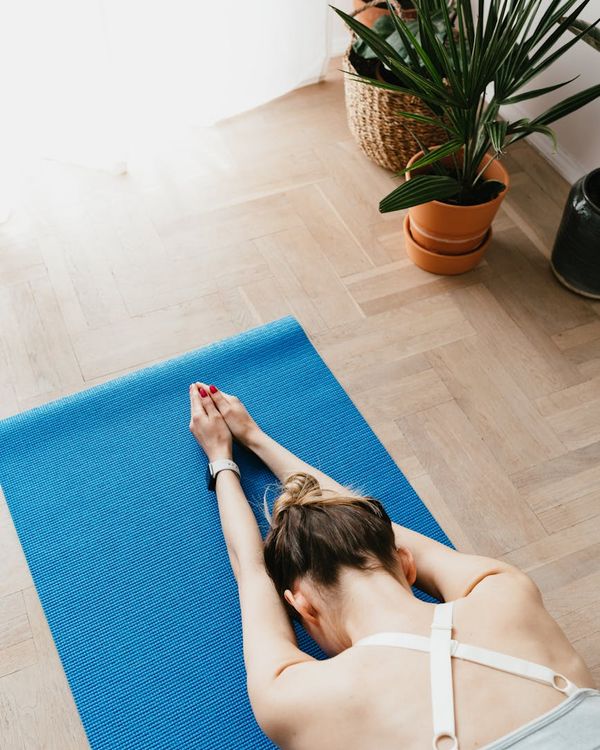 Person stretching on a yoga mat in a sunlit room, view from above.