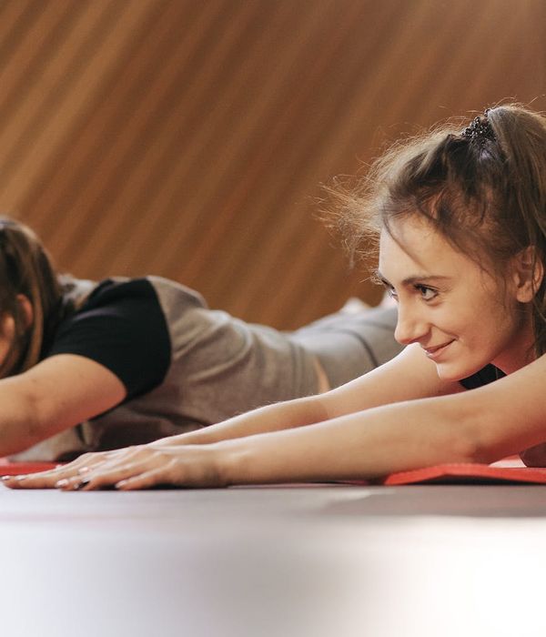 Two women in a bright studio smiling and preparing for a yoga class.